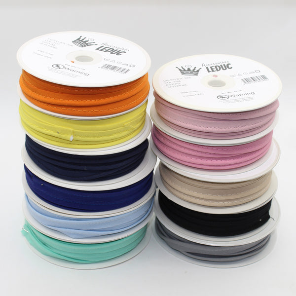 Bobines de biais en coton coloré pour couture et loisirs créatifs, empilées sur fond blanc.